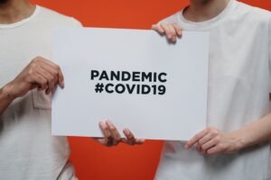 Two people holding a poster with 'Pandemic #COVID19' message on a vibrant background.