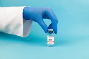 Medical professional hand wearing glove holding COVID-19 vaccine vial against blue background