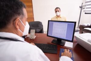 Doctor consults patient remotely using computer and face masks for safety.